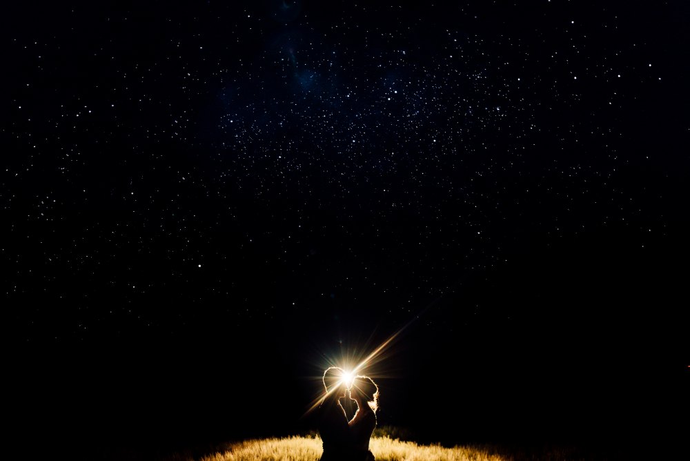 Brautpaar als Silhouette im Gegenlicht unter einem Sternenhimmel auf einem Feld